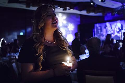A woman in a black dress holds a candle during an event